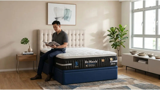 Man reading on a Dr Maxis mattress in a bright Singapore bedroom with plant, side table, and window