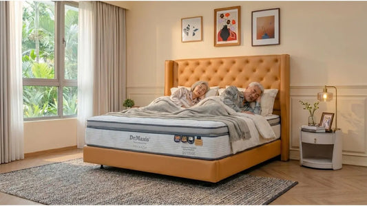 Older couple sleeping on a Dr Maxis queen mattress with tan upholstered bed frame in a bright bedroom