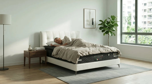 Older adult sleeping on an Esteller mattress in a bright bedroom with side table, window, and plant